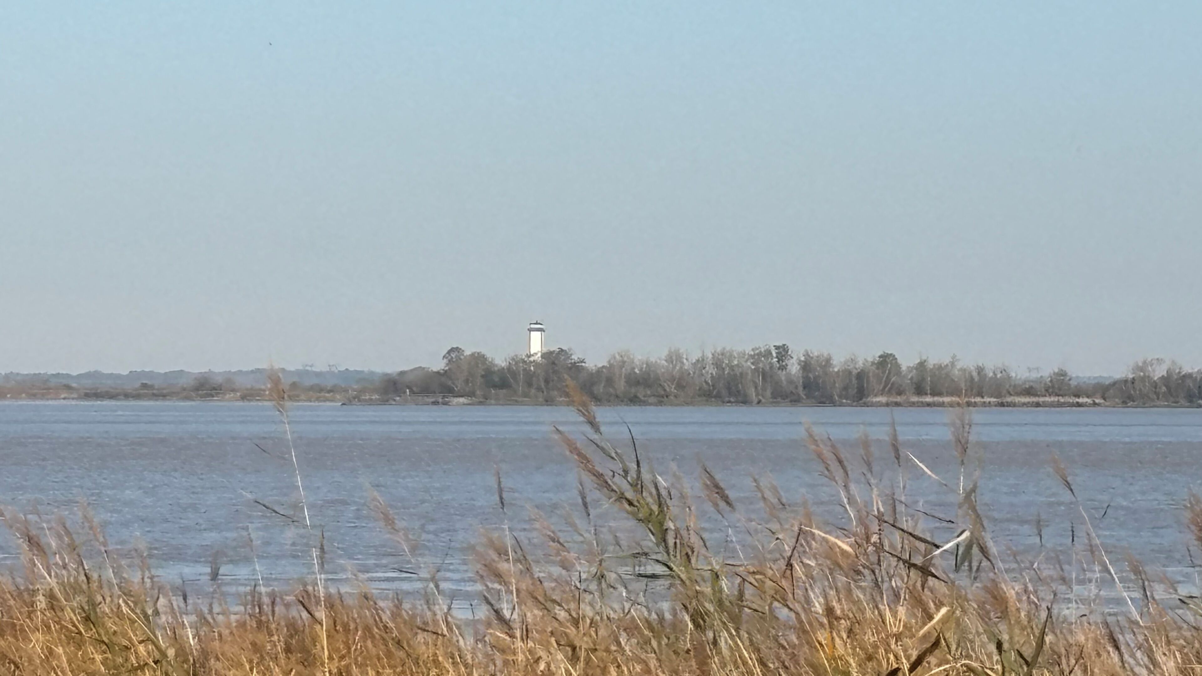 A lighthouse on a distant island across a calm body of water.