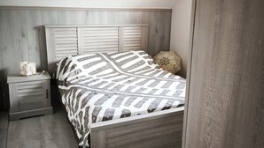 Un dormitorio con cabecera de madera, una cama con ropa de cama estampada, una mesita de noche con lámpara y suelo de madera.