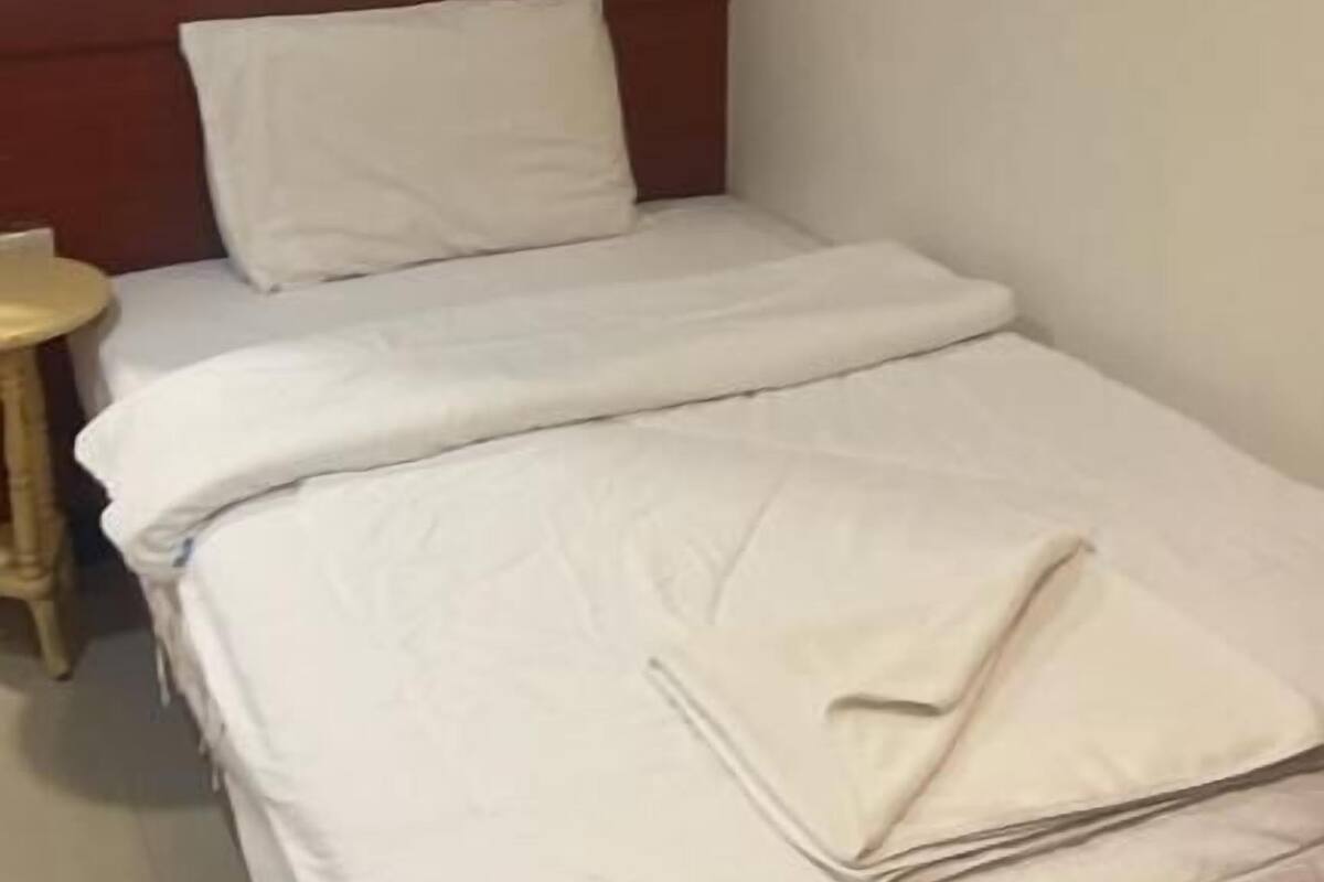 A single bed with white bedding in a room with a wooden headboard and a small round table beside it.