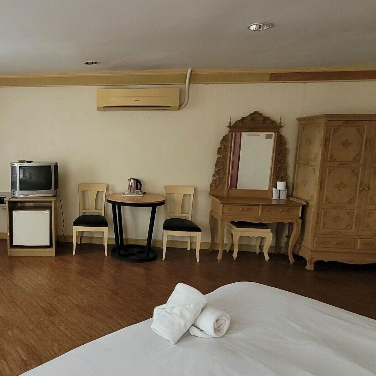 A hotel room with a bed, two chairs, a small table, a television, a mirror, and a wardrobe.