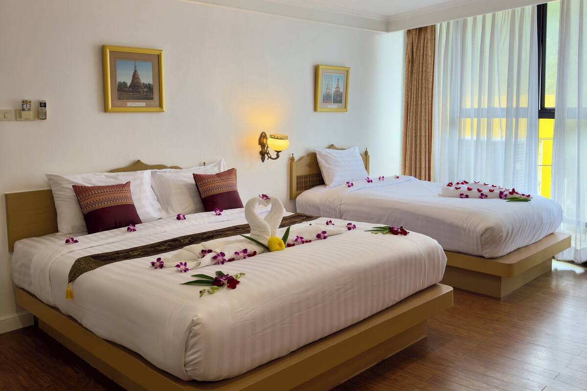 A hotel room with two beds, wooden flooring, and a large window with sheer curtains.