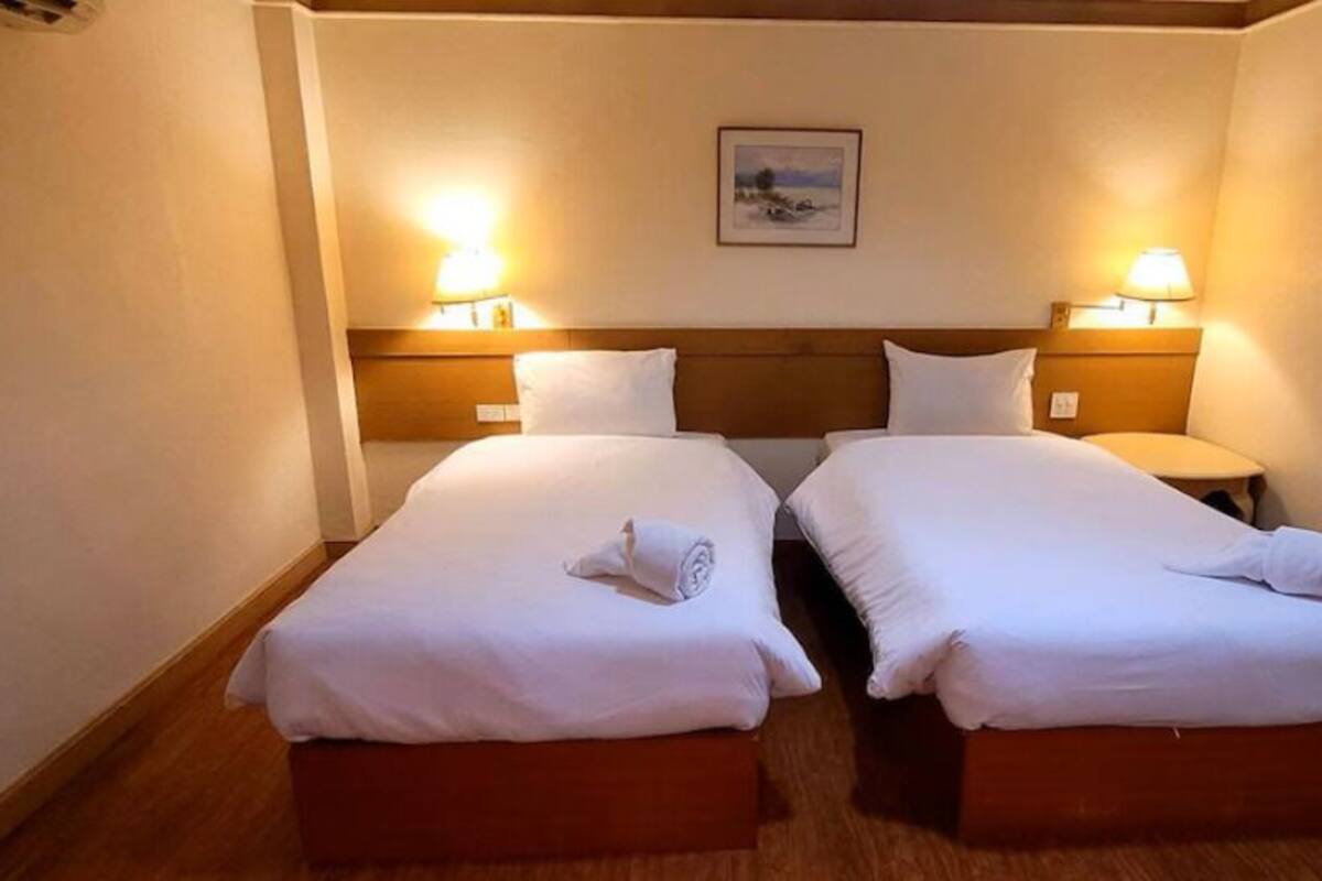 A hotel room with two beds, each with a wooden headboard, white linens, and a pair of bedside lamps.