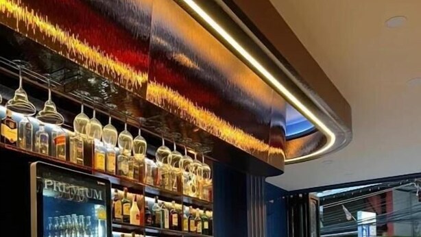 A bar area with a dark counter, shelves of bottles, and bar stools. - Neptuna Kata Beach Phuket (Karon)