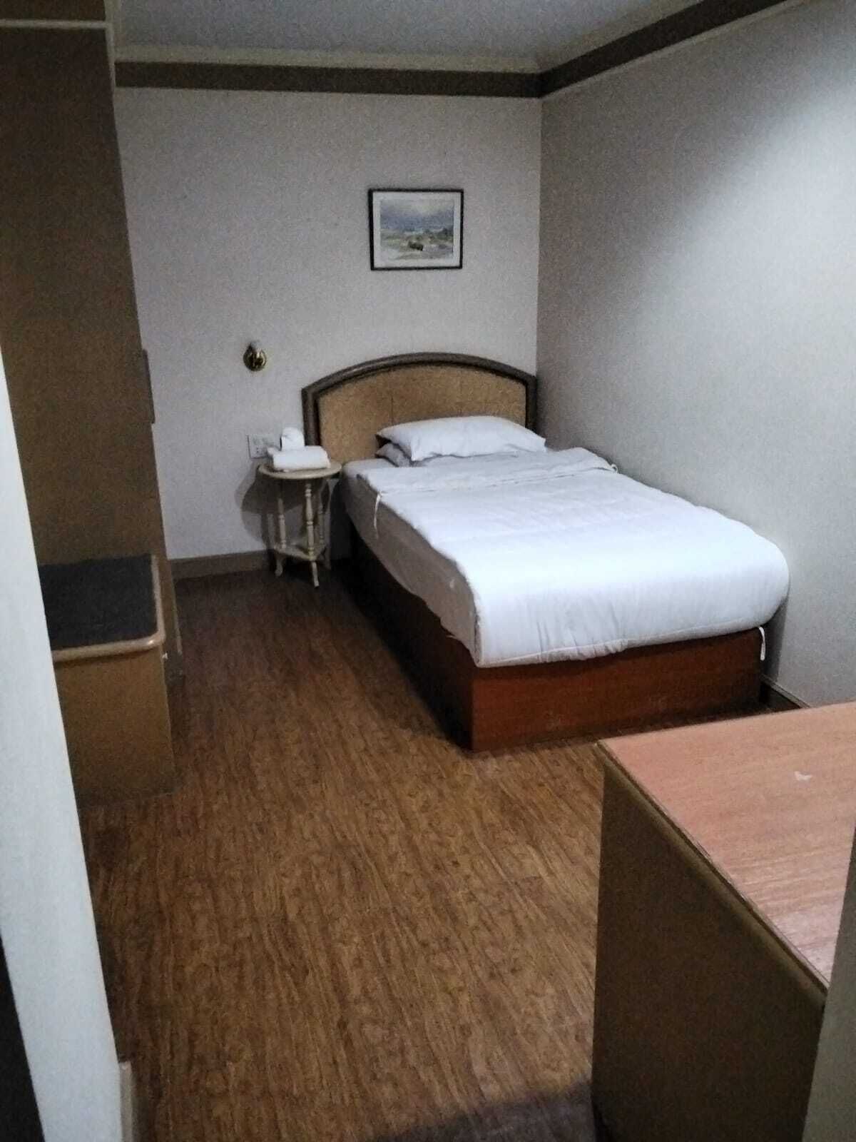 A hotel room with a bed, a bedside table, a small table with a chair, and a wardrobe.