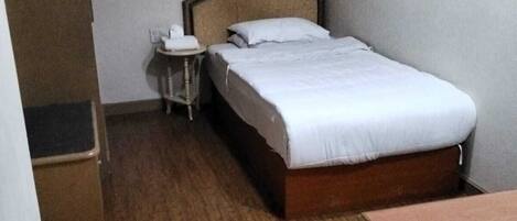 A hotel room with a bed, a bedside table, a small table with a chair, and a wardrobe.