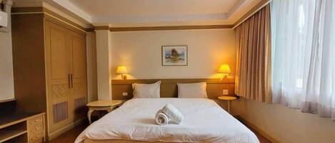 Un cuarto de hotel con una cama grande, dos mesitas de noche con lámparas, un armario y un cuadro en la pared.