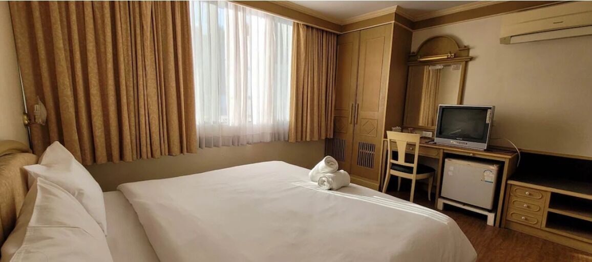 A hotel room with a large bed, a desk with a television, and a wardrobe.