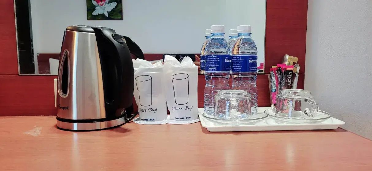 Een hotelkamer met een waterkoker, twee glazen zakken, waterflessen, en een dienblad met glazen en een kopje.