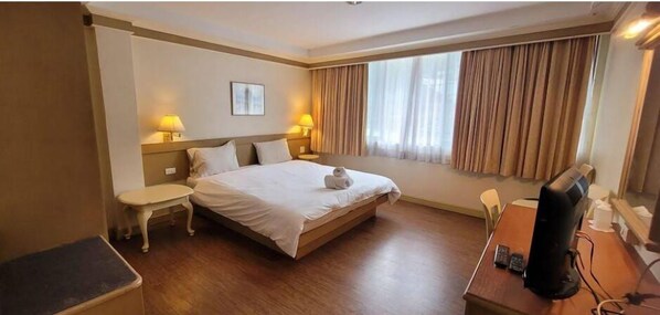 Una camera d'hotel con un letto, comodini, una scrivania con un computer e una finestra con tende.