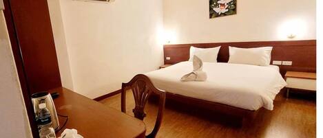 A hotel room with a bed, bedside table, chair, and an air conditioning unit.