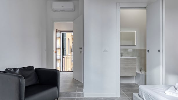 A modern bedroom with a black leather sofa, a bed, and a bathroom with a mirror and sink. - BluesHouse Carracci Suites (Bologna)