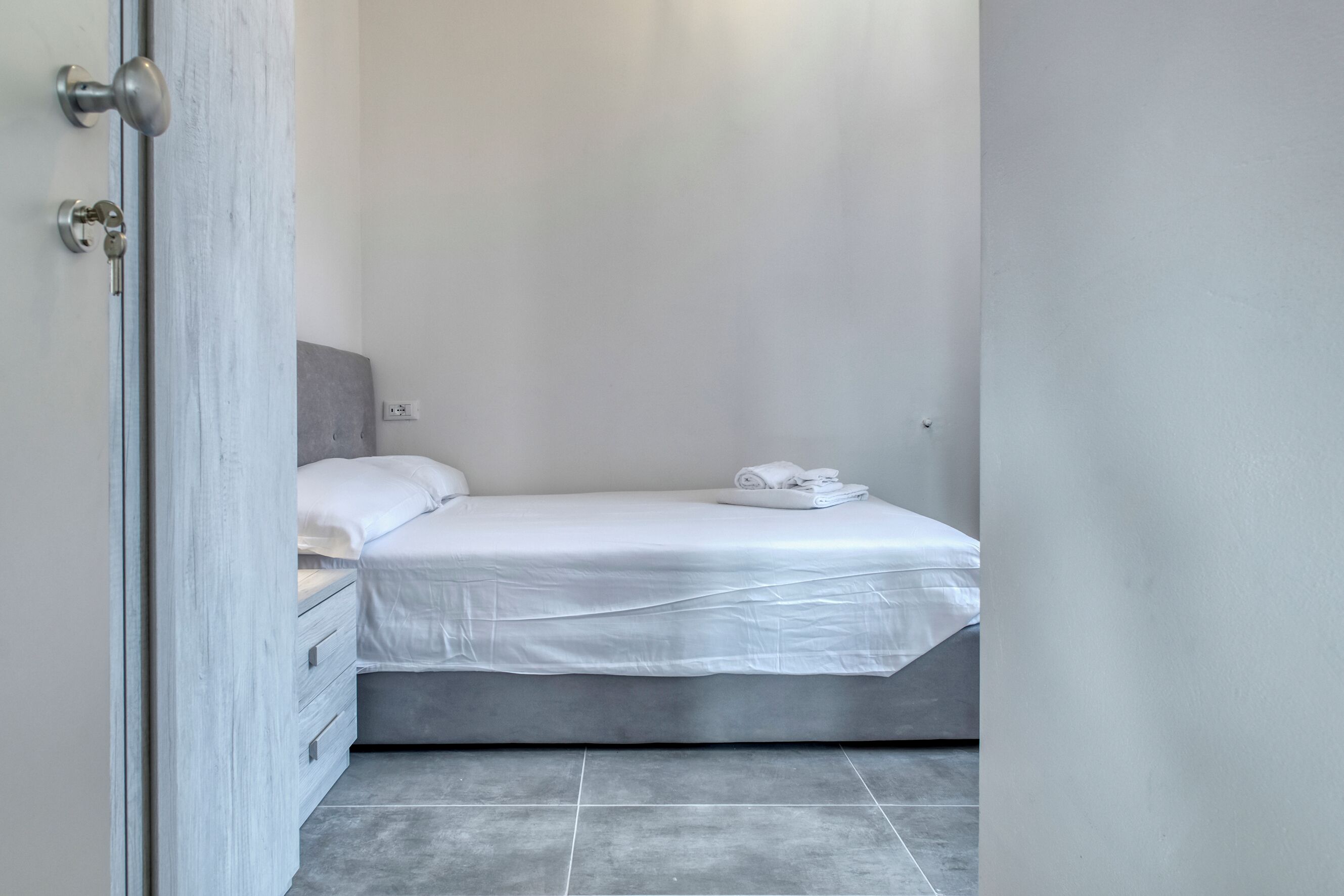 Un dormitorio con cama, mesita de noche y puerta.