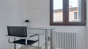 A room with a black leather chair, a glass table, a window with a view of buildings, and a white radiator. - BluesHouse Carracci Suites (Bologna)