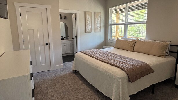A bedroom with a bed, a window with blinds, a door, and a bathroom visible through an open door. - Secret Gem- Spacious Lakefront 8bdrm-20 beds-Sleeps 34. Celebrate Holidays Here! (Lafollette)