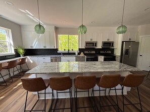 A modern kitchen with a large island, bar stools, stainless steel appliances, and pendant lights.