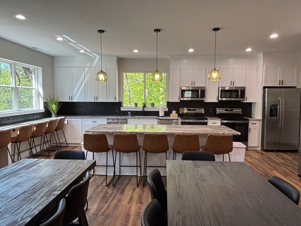 A modern kitchen with white cabinets, stainless steel appliances, a central island with bar stools, and pendant lighting.