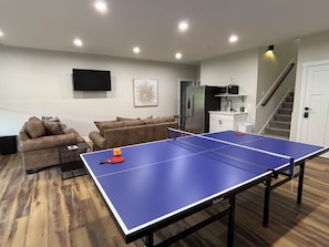 A living room with a ping pong table, a sofa, a TV, and a kitchen area.