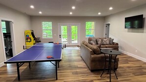 A room with a ping pong table, a sofa, and a TV mounted on the wall. - Secret Gem- Spacious Lakefront 8bdrm-20 beds-Sleeps 34. Celebrate Holidays Here! (Lafollette)