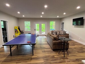 A room with a ping pong table, a sofa, and a TV mounted on the wall. - NEW! LakeFront, 20 beds-sleeps 34, Dbl Deck Dock w/Slide; Theater Rm; Ice Maker (Lafollette)
