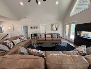 A spacious living room with a sectional sofa, a black coffee table, and a large TV.