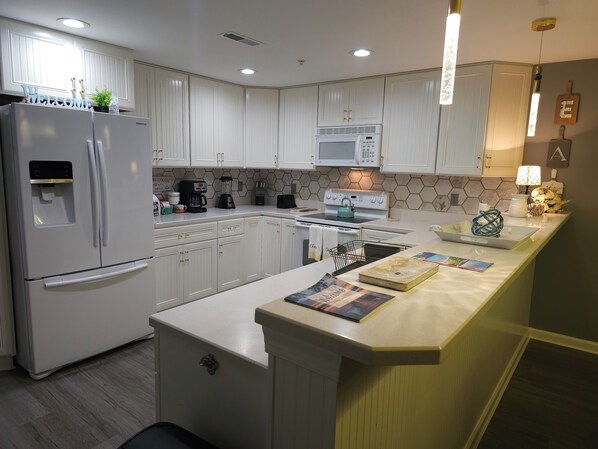 Una cocina moderna con armarios blancos, horno integrado, microondas y refrigerador.