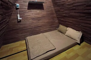 Una habitación pequeña con una cama, estante en la pared y toma corriente.