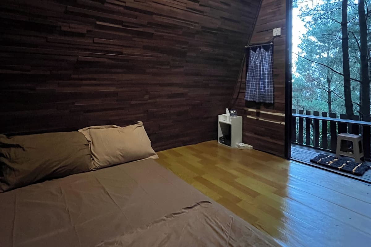 A bedroom with a wooden floor and a bed with beige bedding.