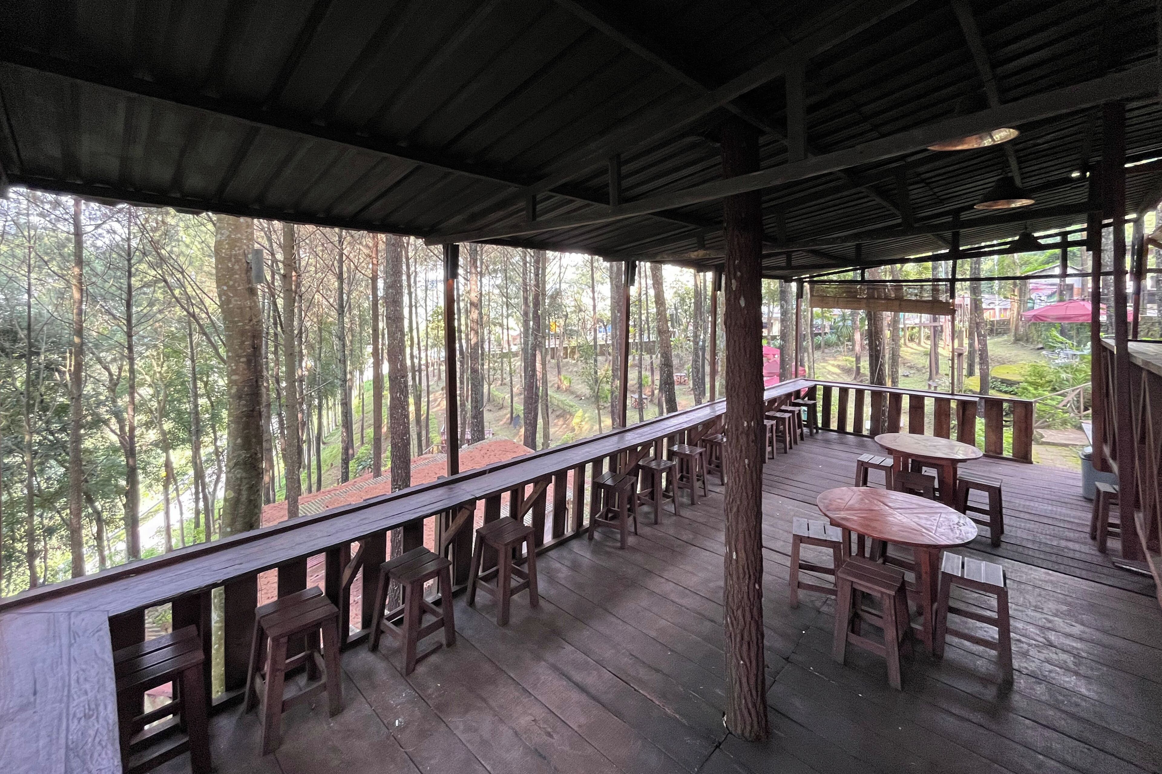 A covered outdoor seating area with wooden tables and chairs, surrounded by trees.