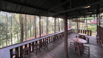A covered outdoor seating area with wooden tables and chairs, surrounded by trees.