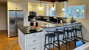 A modern kitchen with white cabinetry, stainless steel appliances, and a central island with bar stools. - Three Peaks Hideaway, a Tranquil 4-bedroom house with Mountain Views in Peru (Peru)