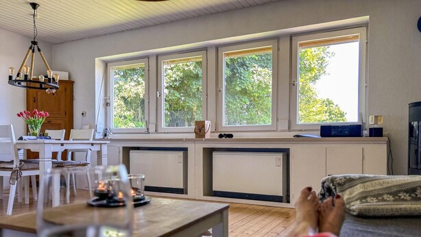 Eine moderne Küche mit drei großen Fenstern, einem Essbereich mit Tisch und Stühlen sowie einem gemütlichen Wohnbereich mit einer Couch.
