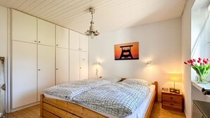 Ein Schlafzimmer mit einem hölzernen Bett, einem Kleiderschrank, einem Wandbild, einem Nachttisch und einer Blumenvase.