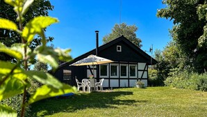 Ein traditionelles Fachwerkhäuschen mit einer kleinen Terrasse, einem Tisch mit Stühlen und einem großen Sonnenschirm.