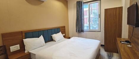 Habitación de hotel con cama, escritorio, silla, aire acondicionado, ventana con cortinas y televisor.