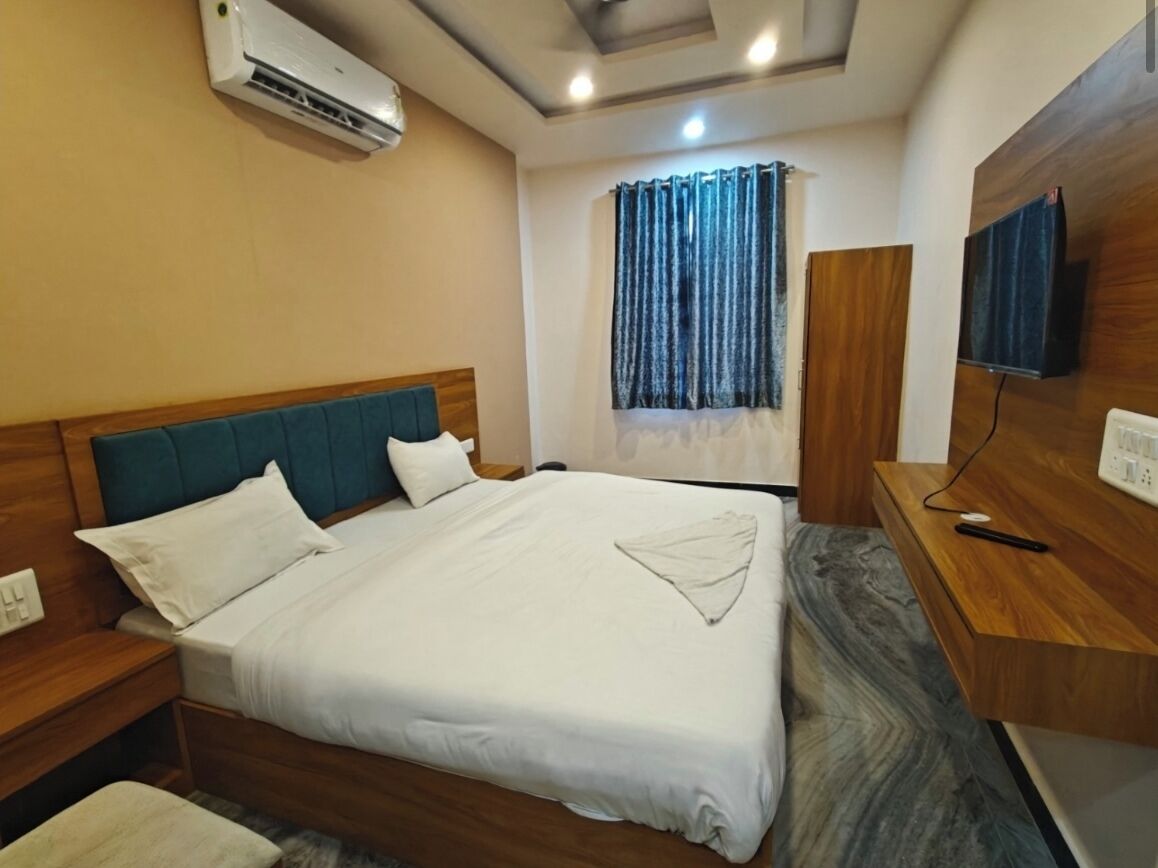 A hotel room with a bed, bedside tables, a TV, and a window with curtains.