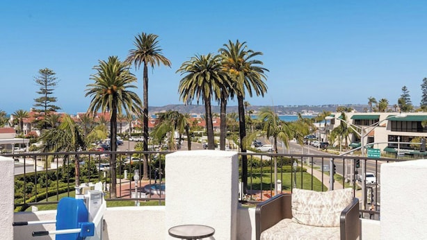 A balcony with a view of palm trees, a pool, and a distant cityscape. - Celebrate winter holidays at the lovely, warm, welcoming Coronado Beach Resort! (Coronado)