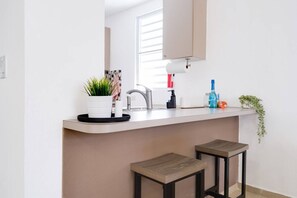 A modern kitchen with a white countertop, a sink, and two stools. - Legacy House on Isla Verde Beach (Carolina)
