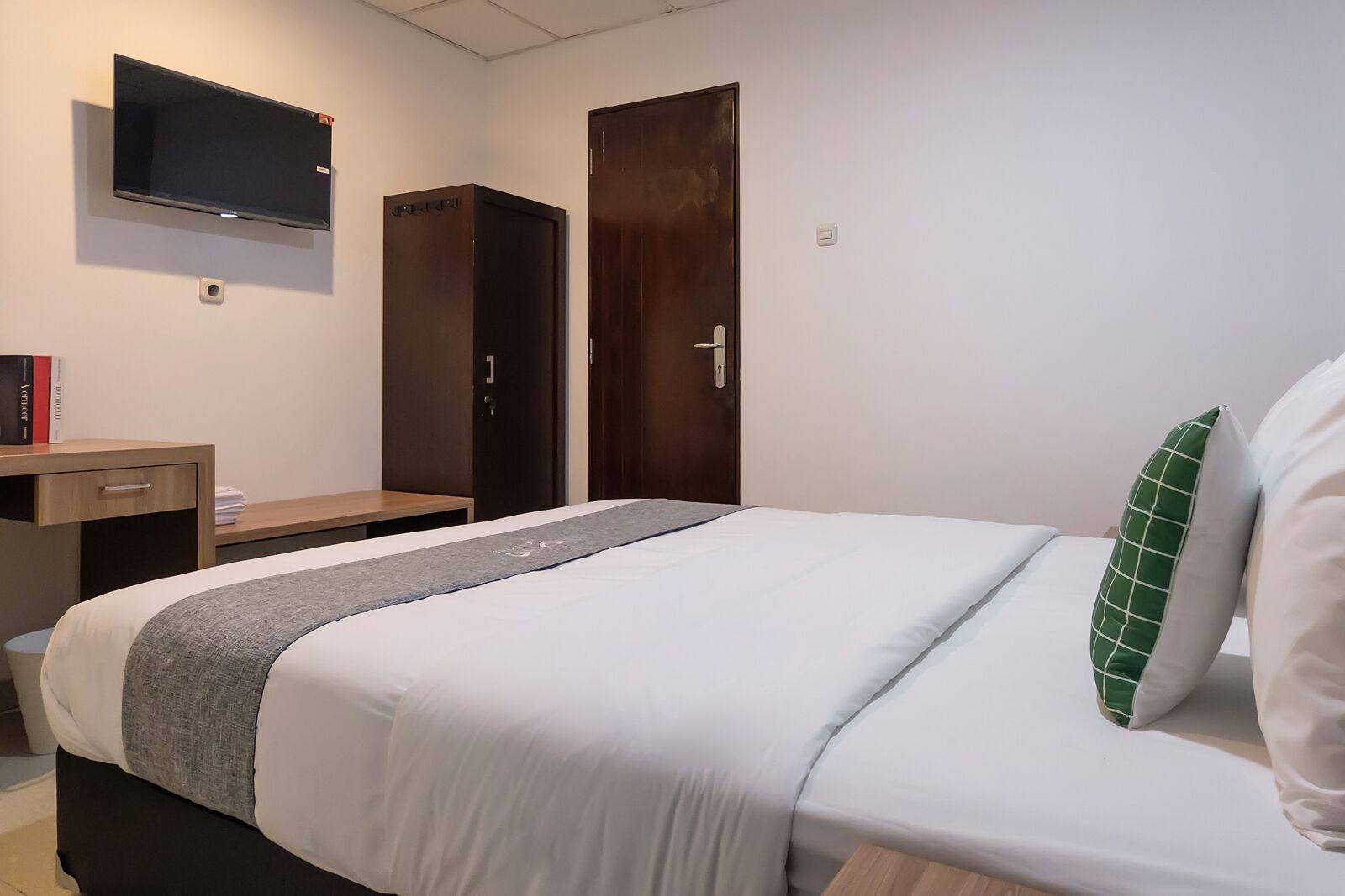 Una camera d'albergo con un letto, una scrivania, un armadio e una TV a muro.