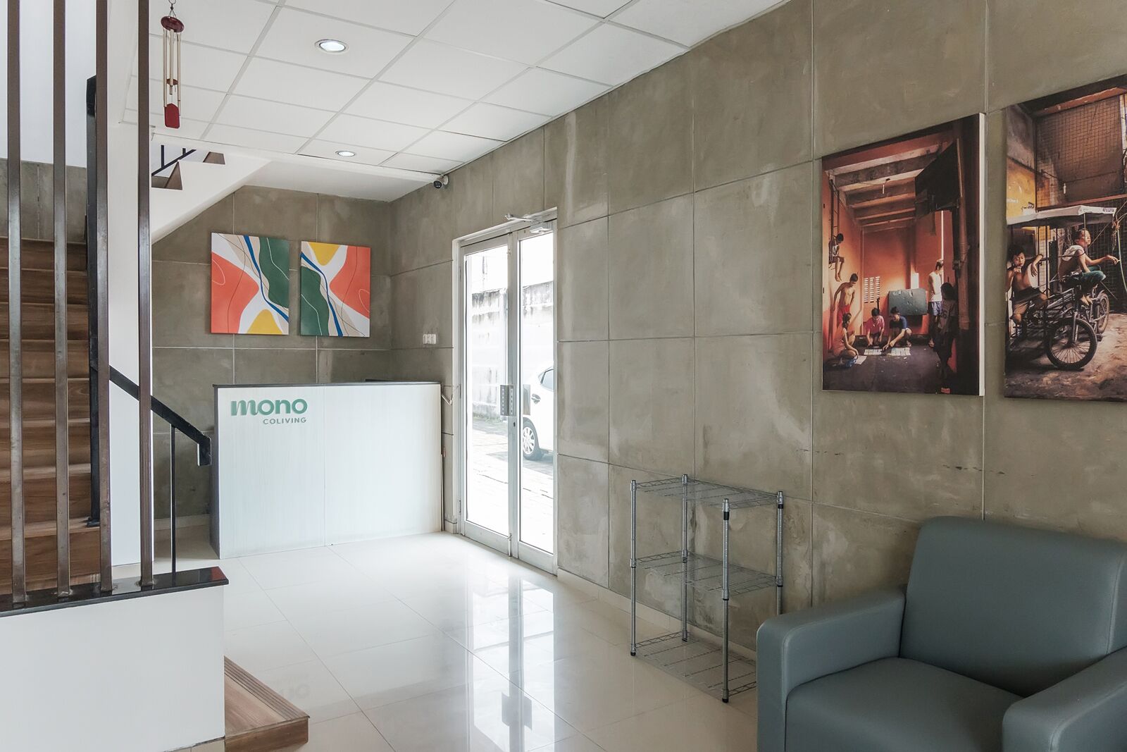 A modern lobby with a reception desk labeled "mono COLIVING," a staircase, and a blue seating area.