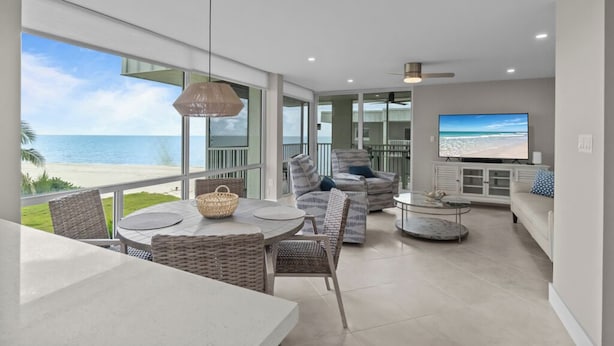 Un amplio salón con un gran ventanal con vistas a la playa, asientos cómodos y un televisor de pantalla plana.