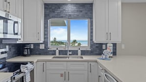 Una cocina moderna con armarios blancos, un salpicadero negro, un ventanal con vista al océano y un microondas empotrado.