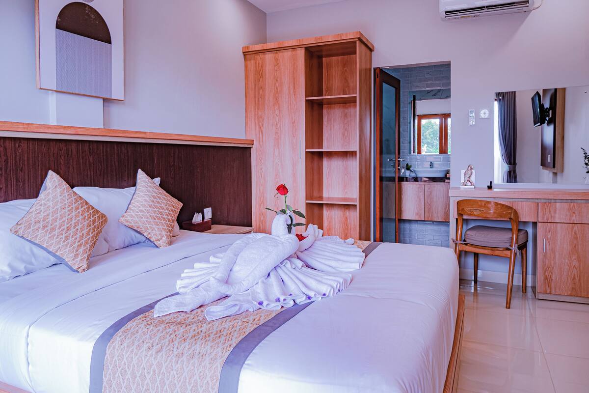 Habitació d'hotel amb un llit gran, un armari de fusta, escriptori i una cadira.