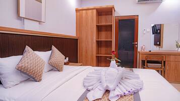 A hotel room with a neatly made bed, a wooden wardrobe, a vanity with a mirror, and an air conditioning unit.