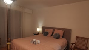 Un dormitorio con cama, lámpara de noche, una silla y un osito de peluche.