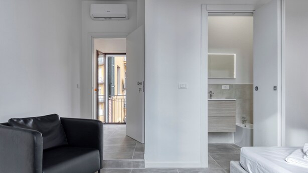 A modern bedroom with a black leather sofa, a bed, and a bathroom with a mirror and sink. - Suite Hendrix | BluesHouse Carracci (Bologna)