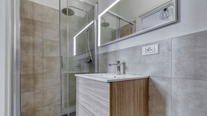 A modern bathroom with a glass shower enclosure, a wooden vanity with a white sink, and a wall-mounted mirror. - Suite Hendrix | BluesHouse Carracci (Bologna)