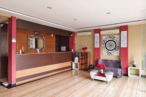 Un espace d’accueil comprenant un comptoir de réception en bois, un grand miroir, un canapé et un élément décoratif mural.
