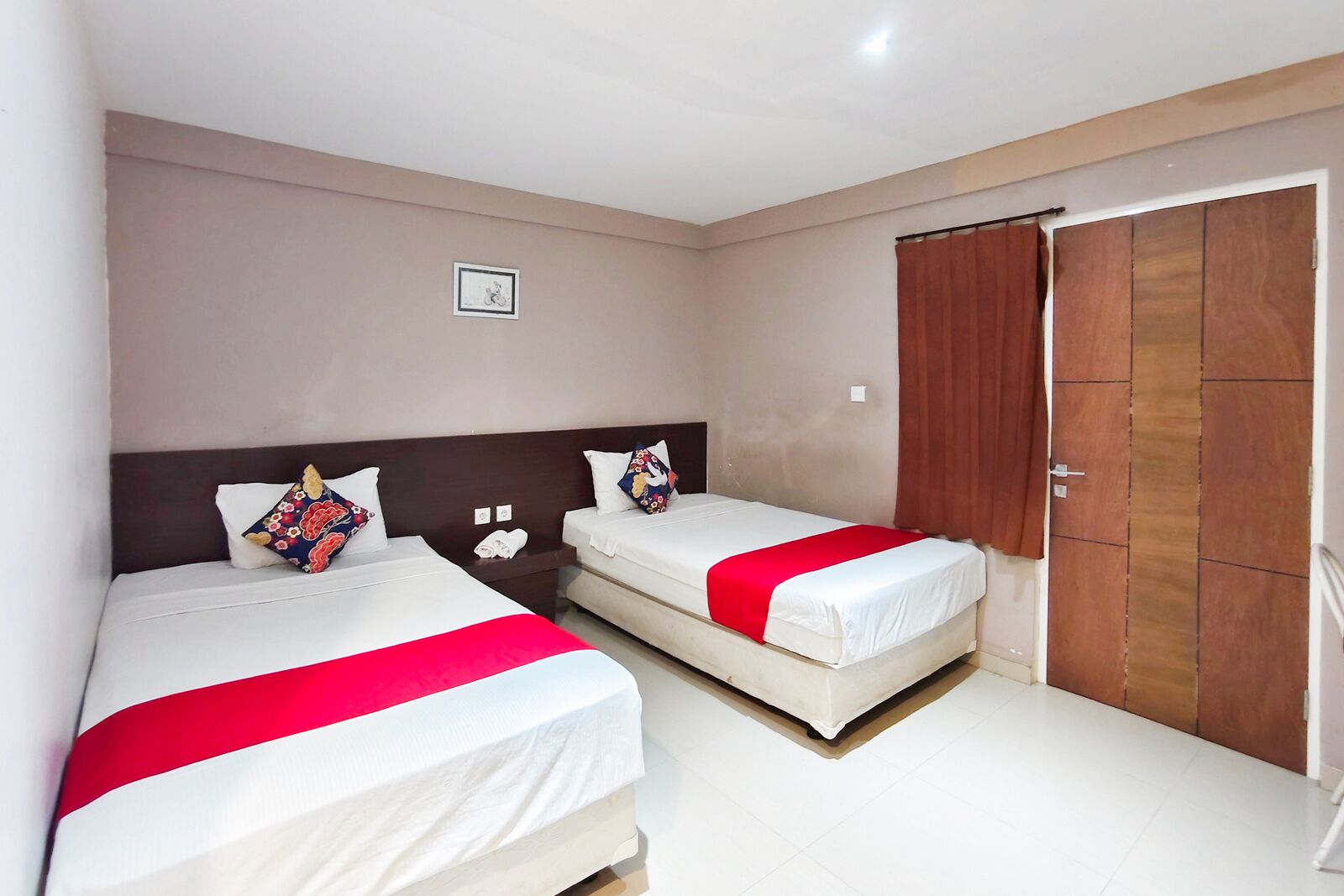 Habitación de hotel con dos camas, un armario de madera y una mesita de noche con lámpara.