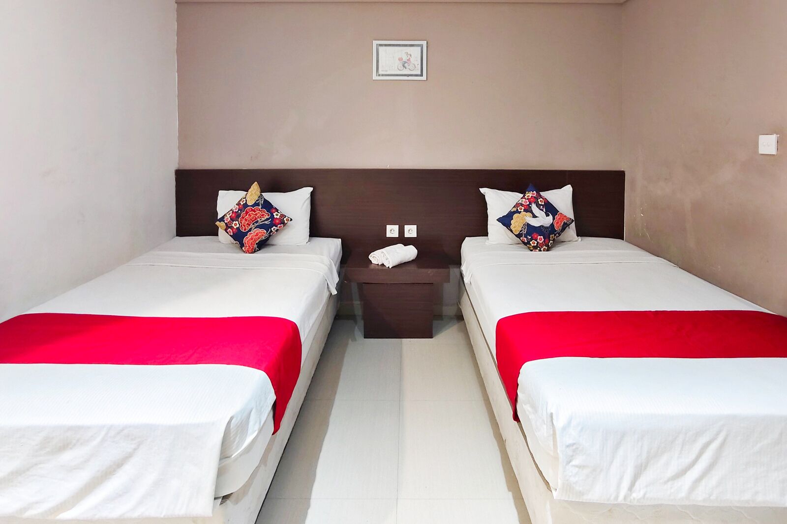 Una habitación de hotel con dos camas individuales, cada una con una colcha roja y blanca, un cabecero de madera y una mesita de noche entre ellas.