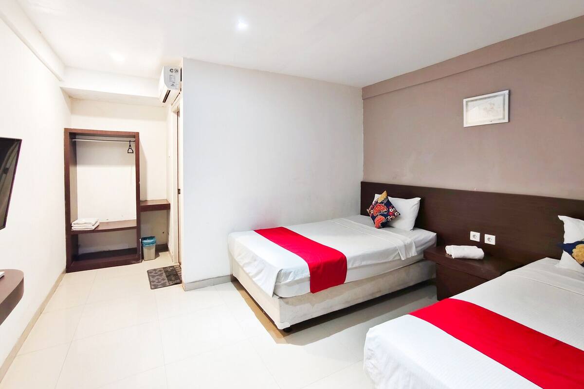 Quarto de hotel com duas camas, um guarda-roupa, um espelho e uma televisão.